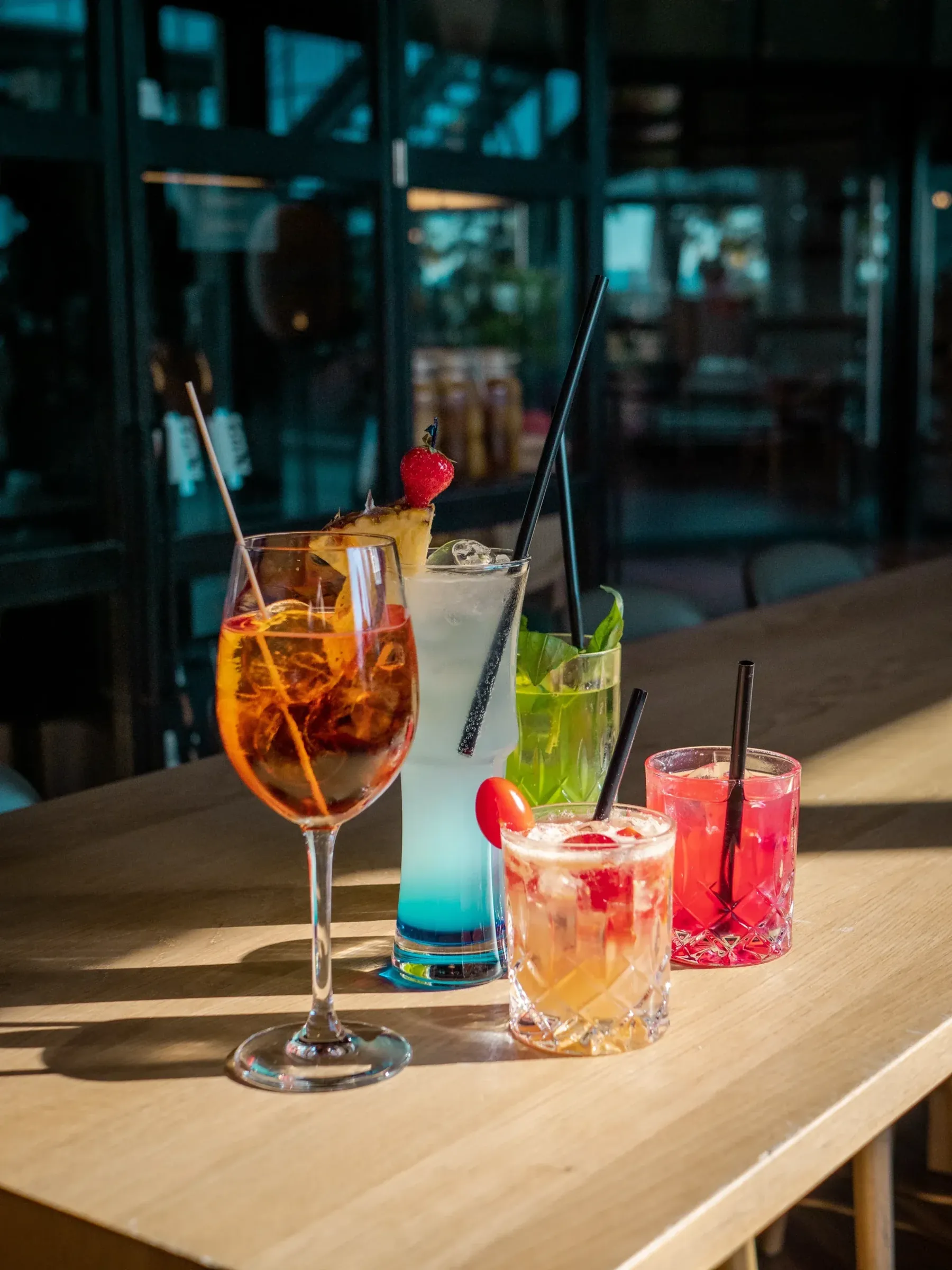 Fünf Cocktails auf einem Holztisch im Gegenlicht