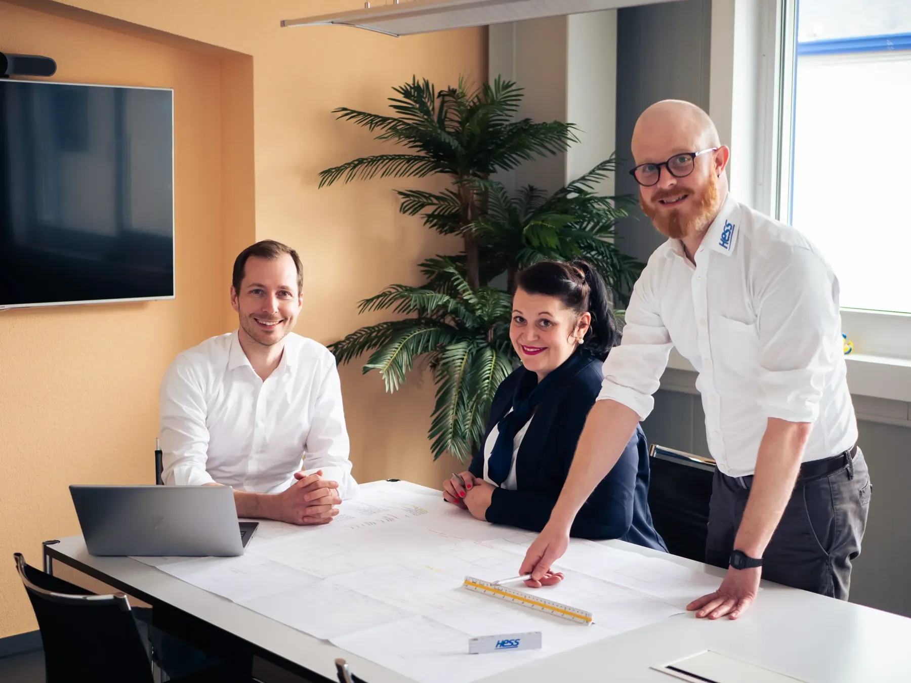 Drei Personen am Besprechungstisch über einem Bauplan
