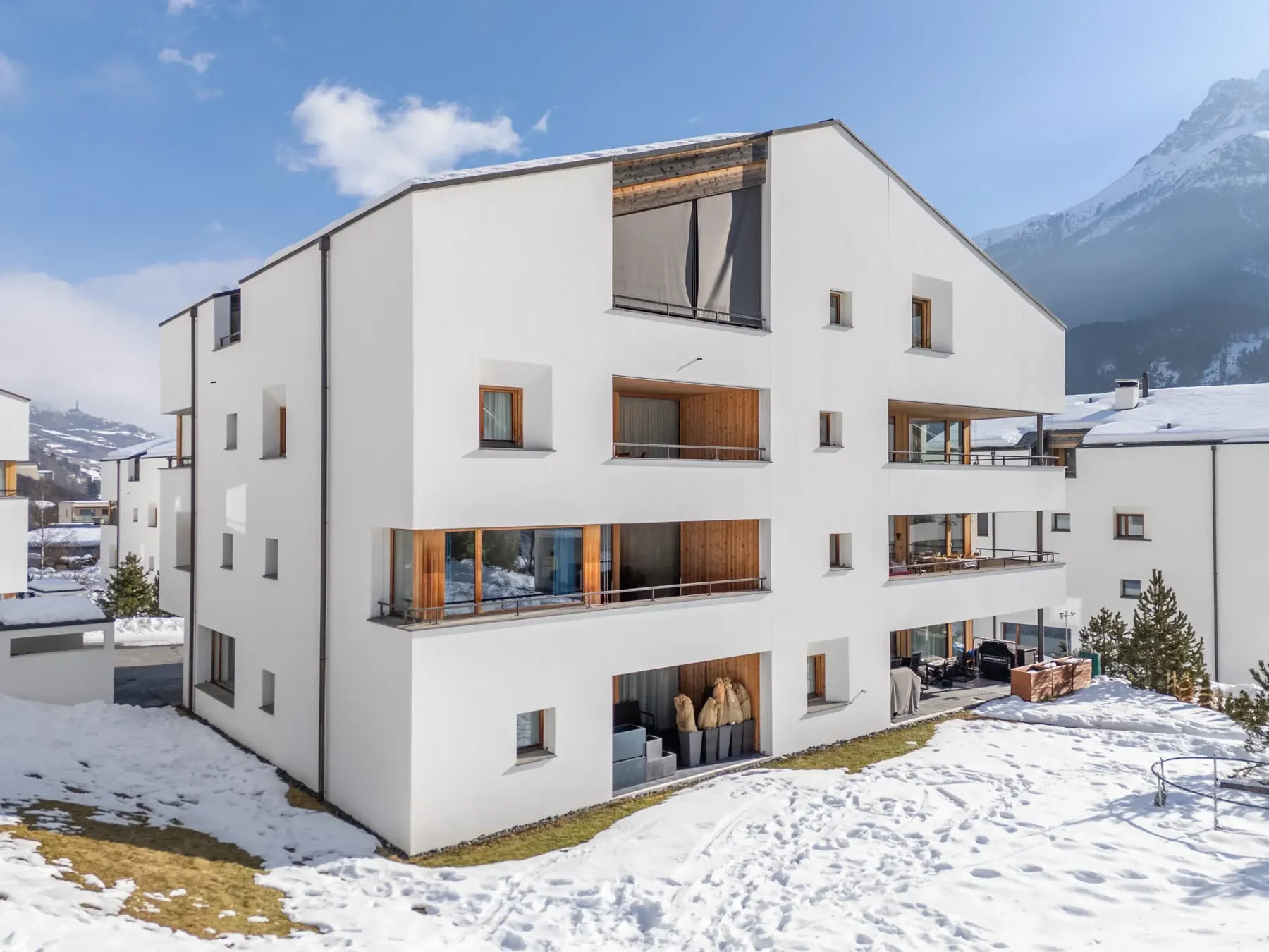 Weisses Mehrfamilienhaus im Schnee vor Bergkulisse