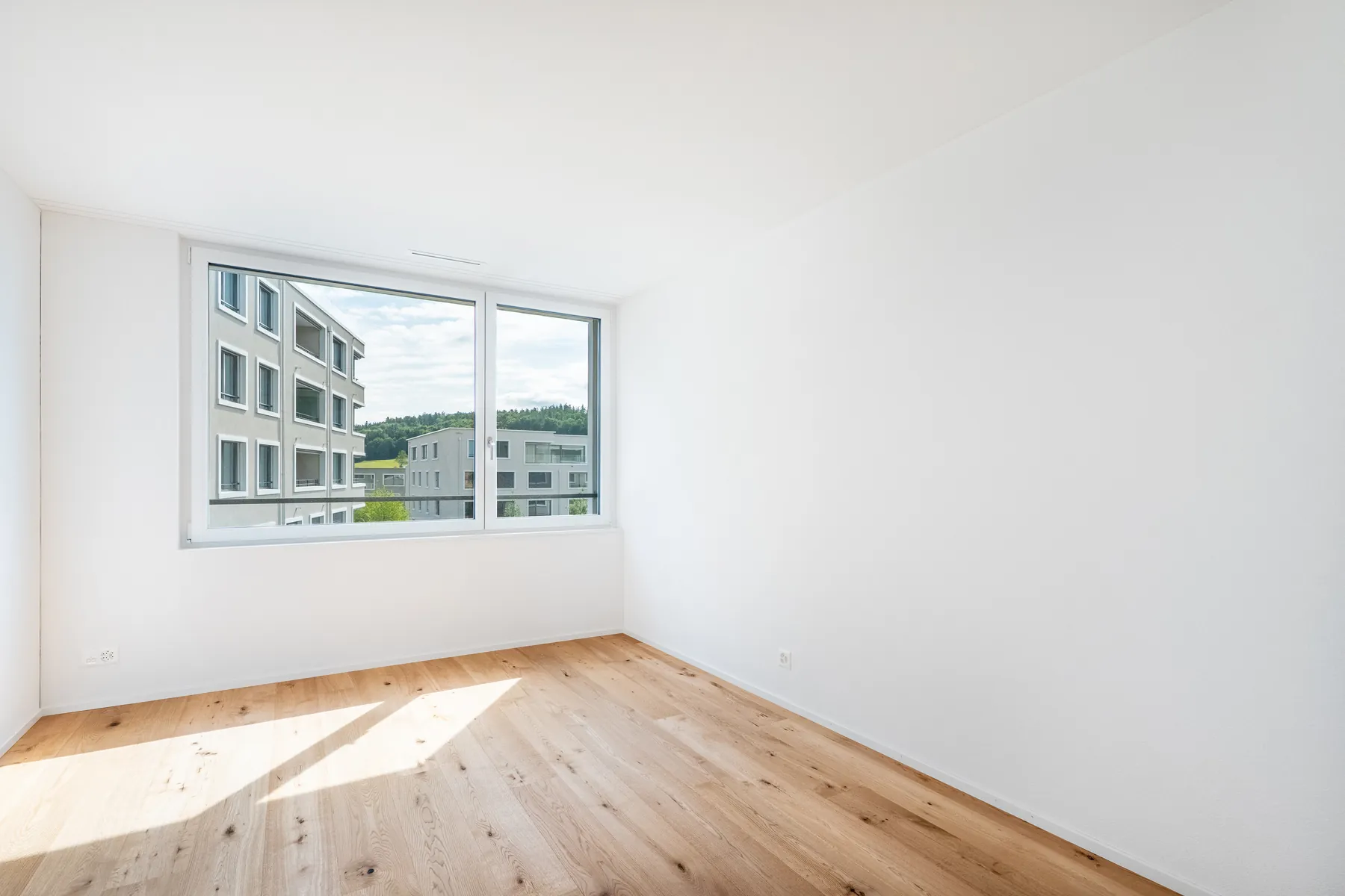 Leerer Wohnraum mit Parkett und Blick auf die Nachbarhäuser
